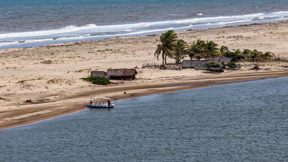 Barco de passeio na barra, entre o rio e a faixa de praia com cabanas