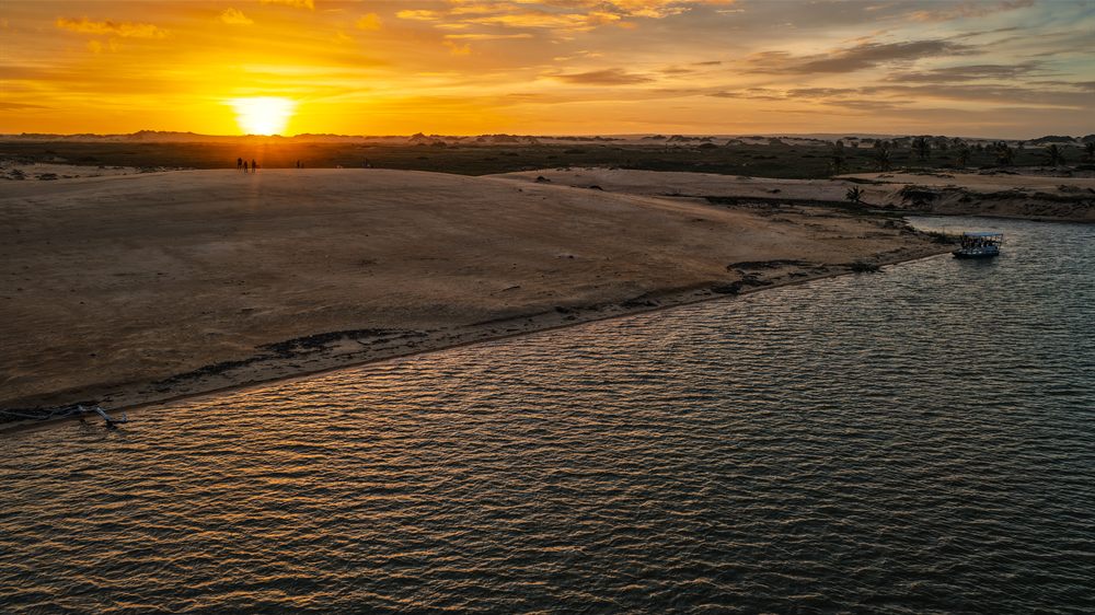 Pôr do sol dourado sobre o rio, com barco na margem